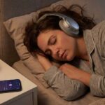 Woman sleeps peacefully in bed wearing headphones near pink light.